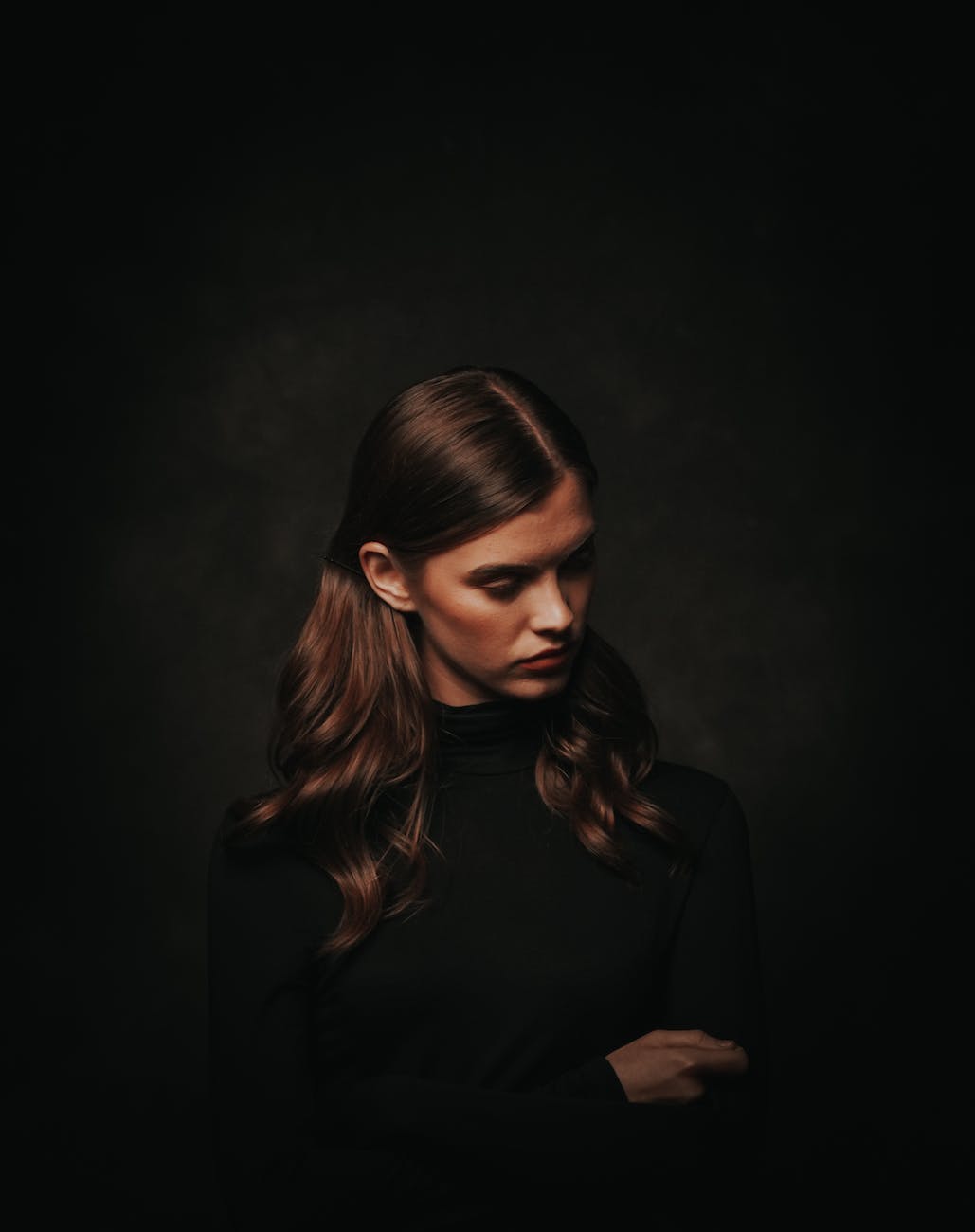 photo of woman in black turtleneck sweater posing in front of black background while looking away
