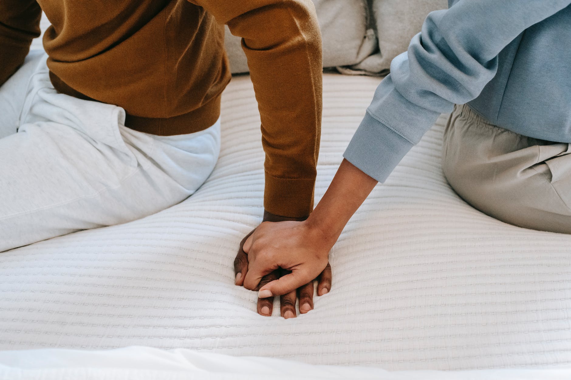 crop unrecognizable black couple holding hands on bed