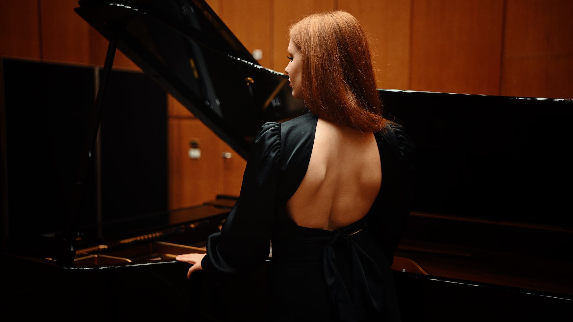 back view of a redhead woman standing by a pianoforte