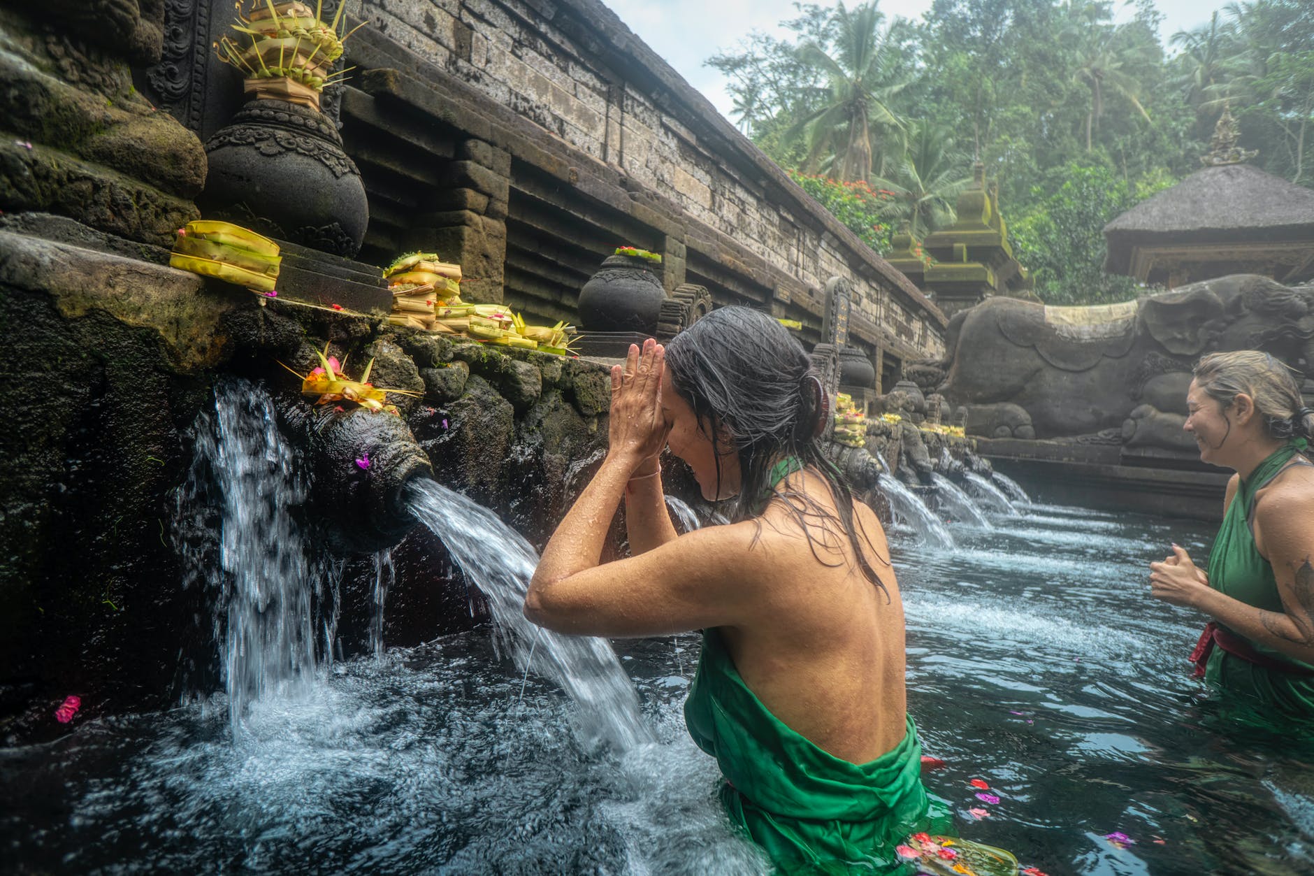women at a spiritual temple praying and cleansing in sacred waterfall pond of temple in jungle. 
